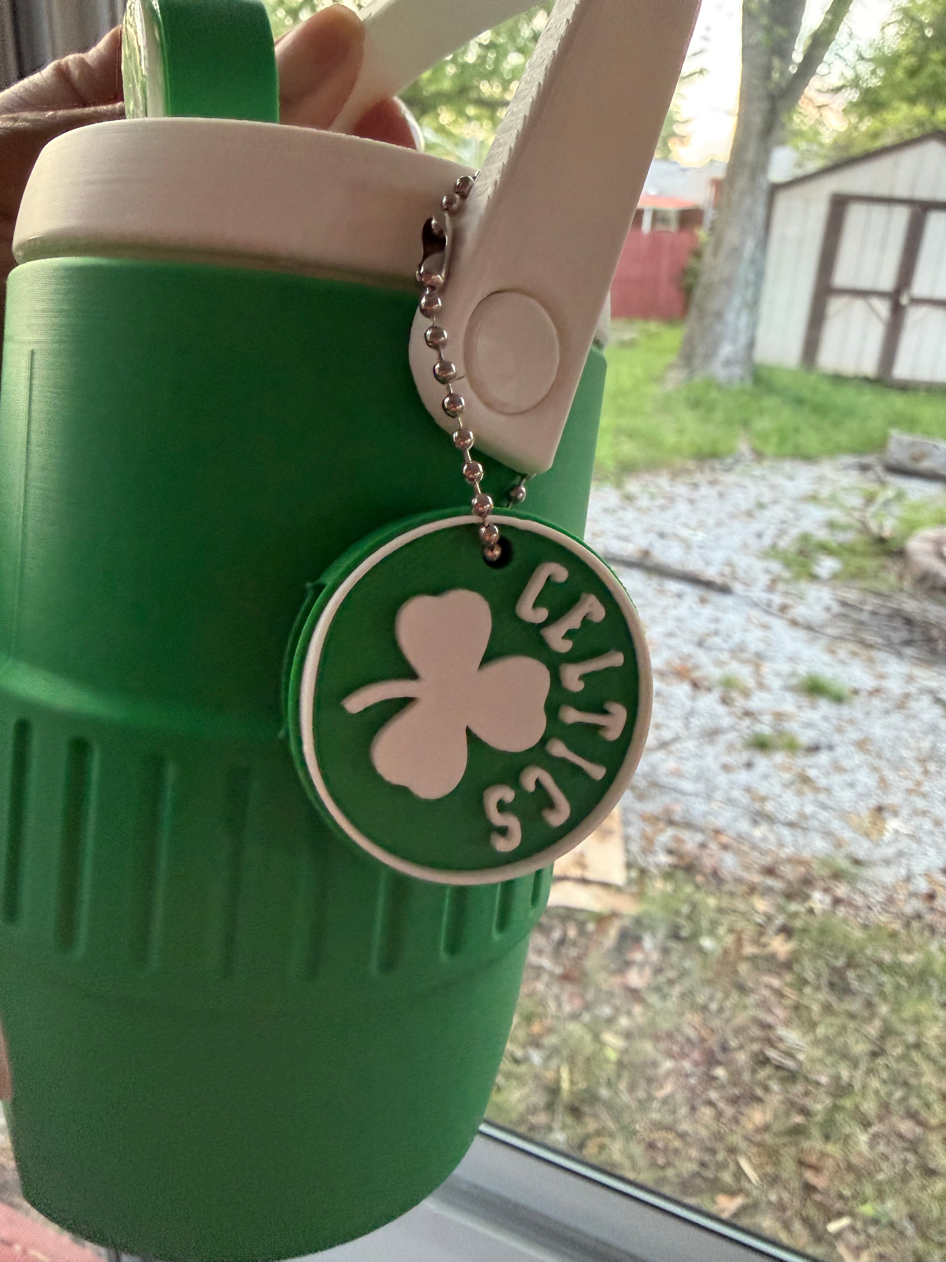Green water bottle with a shamrock logo and 'Celtics' text, held outdoors.