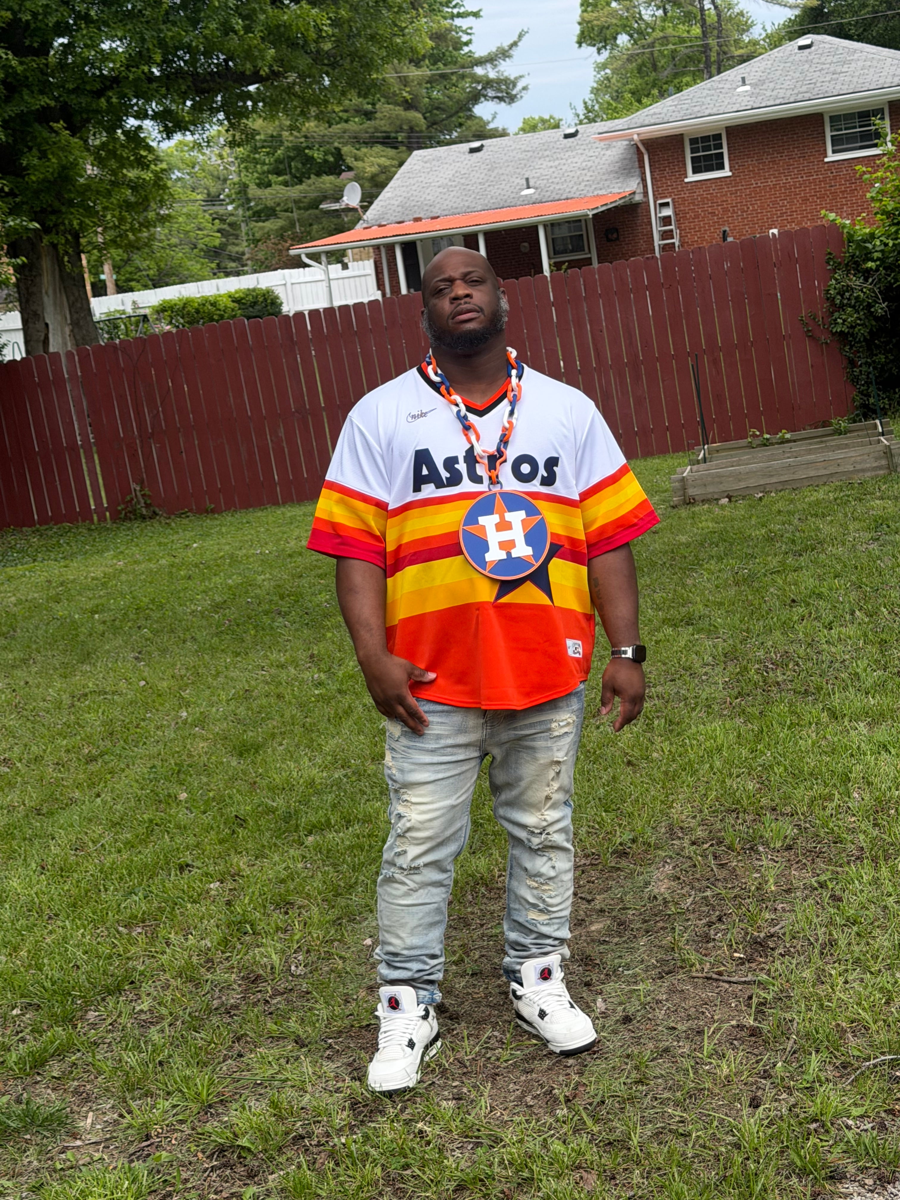 Person wearing an Astros jersey and colorful vest on a grassy area with a building in the background