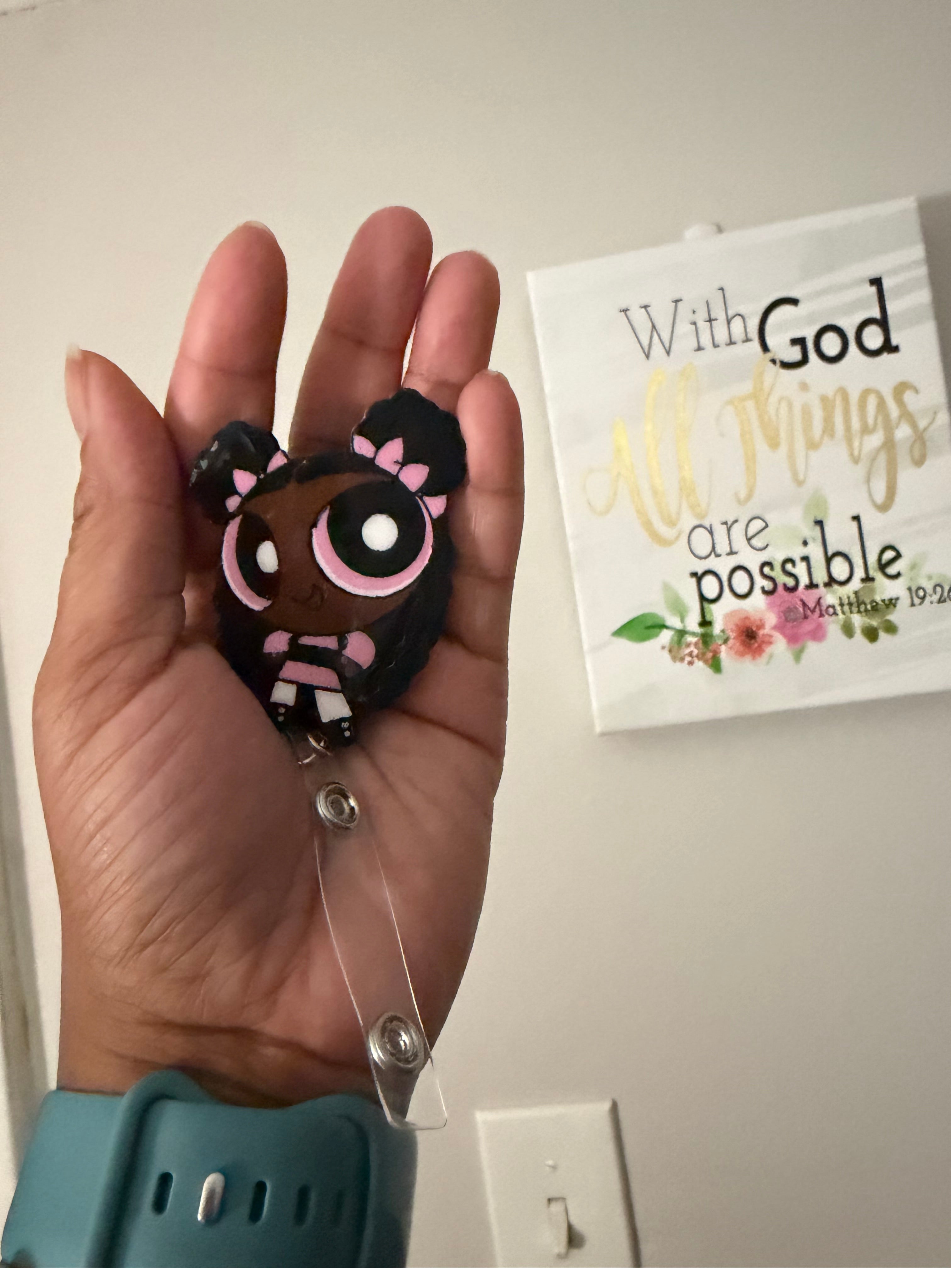 Hand holding a small black and pink object with a clear strap, with a motivational card in the background.