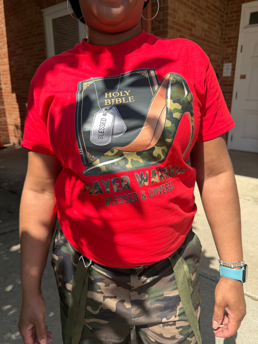 Woman wearing red prayer warrior shirt with heel and matching camo pants 